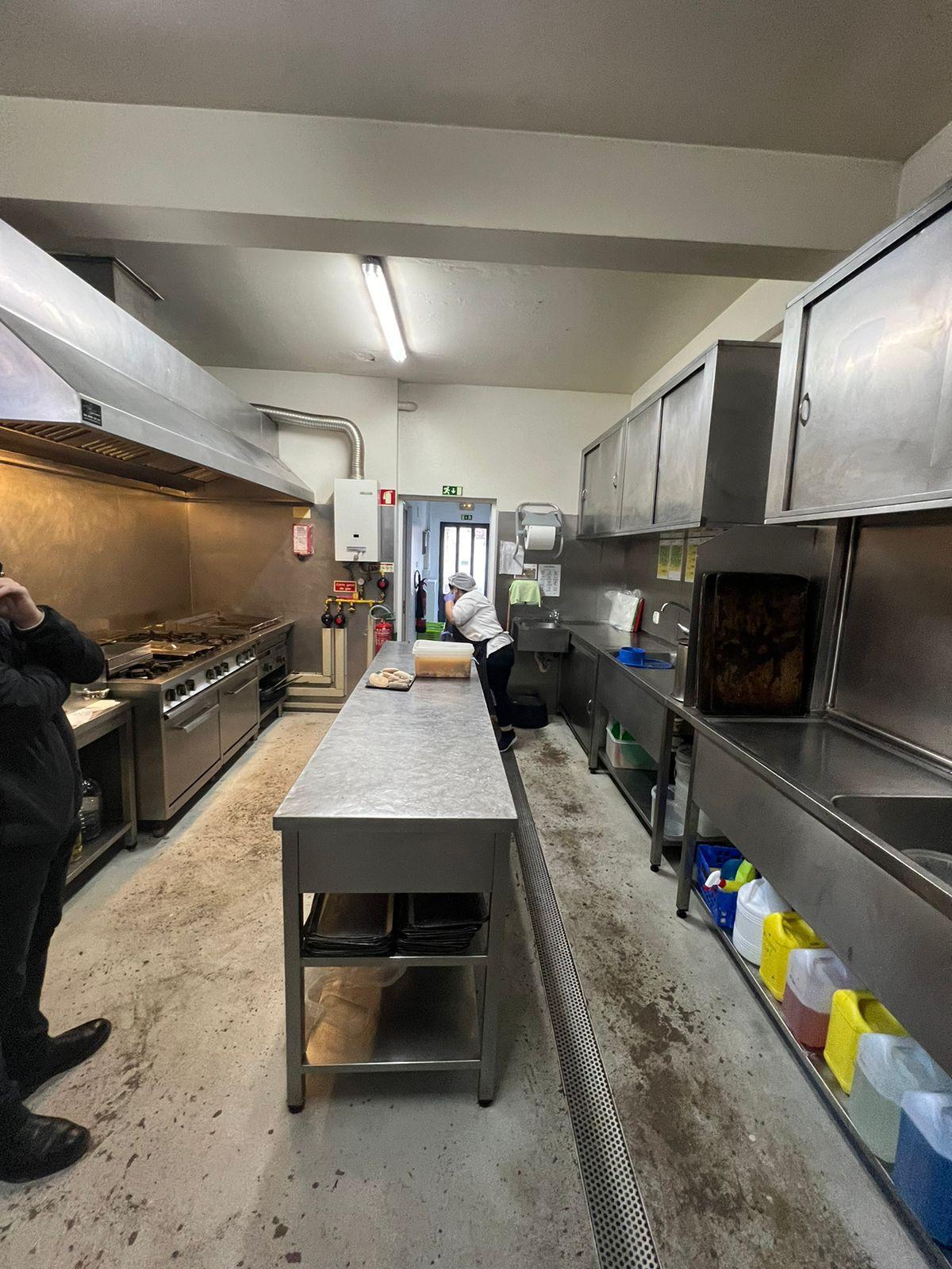 Cozinha original do estabelecimento com bancada em inox, equipamento e zona de preparação.