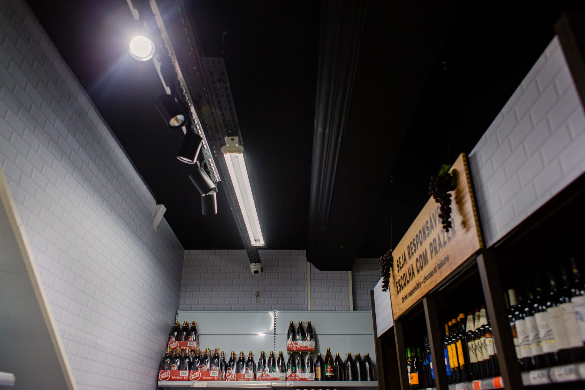 Corredor de bebidas com tecto preto e revestimento em azulejo metro branco.
