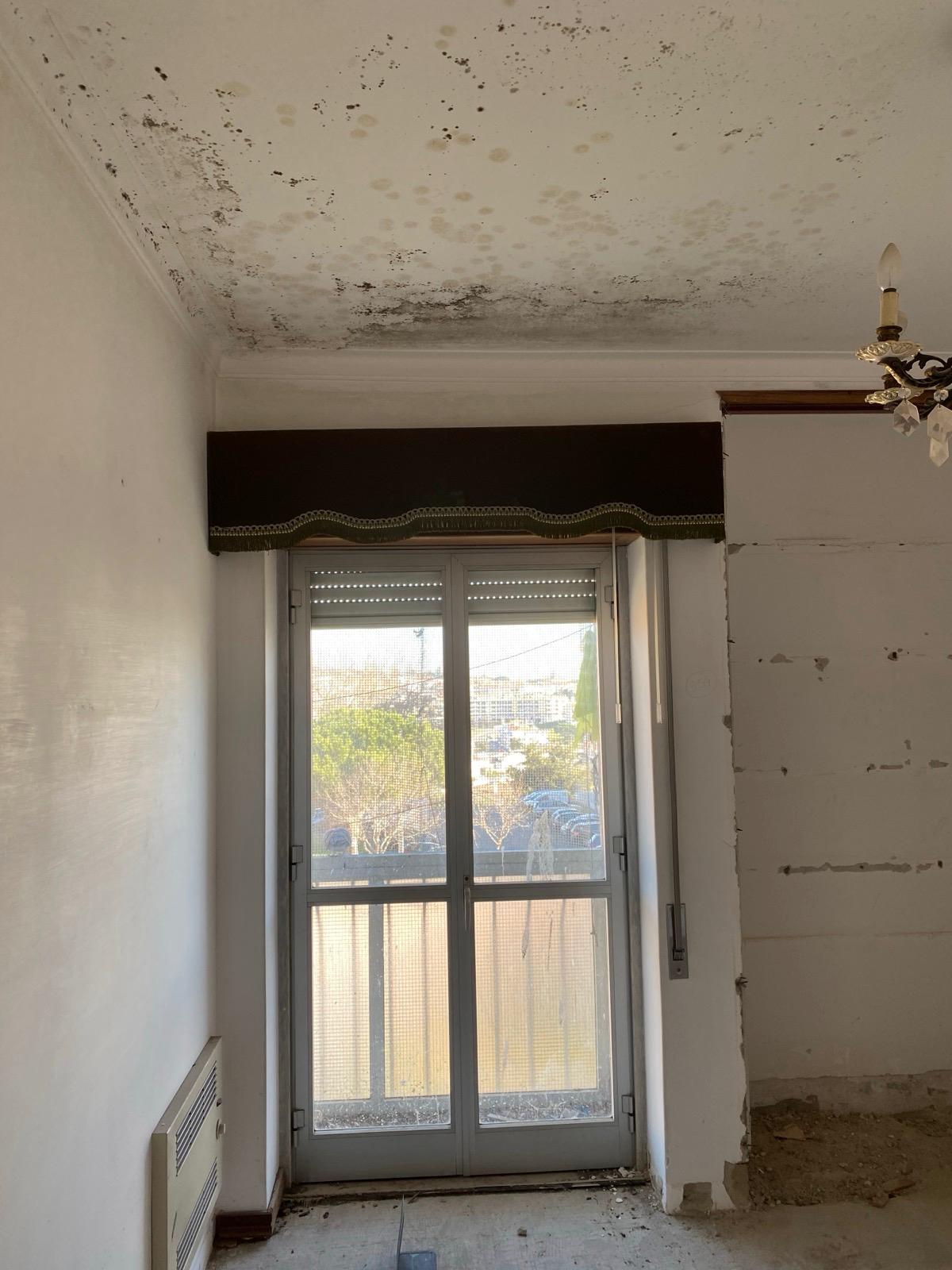 Estado inicial — sala com humidade no tecto, portas com cortinados antigos e candelabro original.